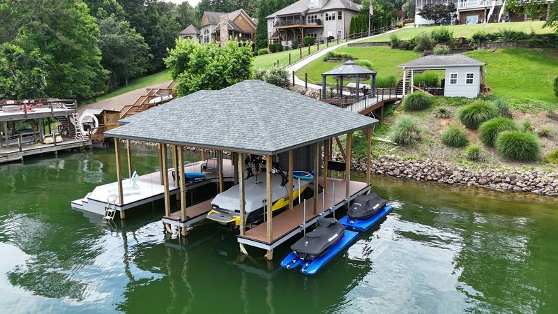 Aerial view of a shingle-roof boathouse with a lifted wake boat and two PWC ports