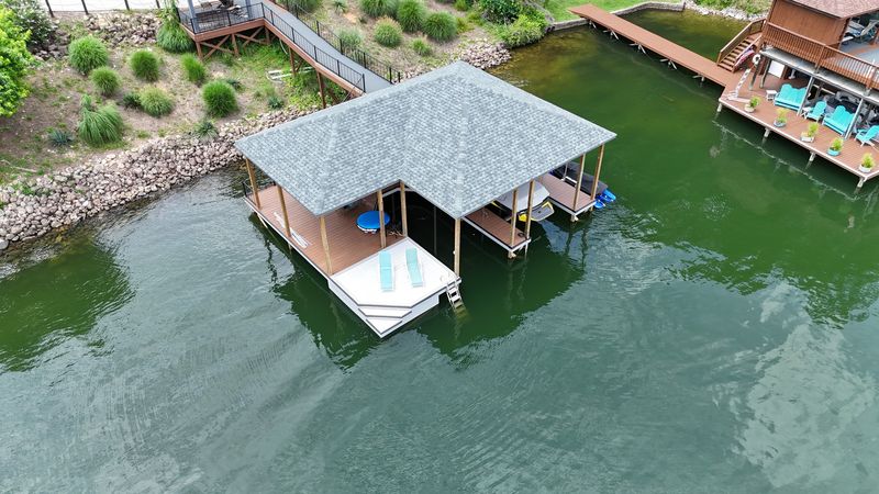 Overhead view of a shingle-roof boathouse beside a riprap shoreline