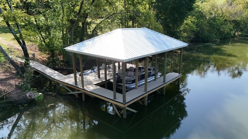 Covered pontoon slip with a white metal hip roof and an angled walkway to shore
