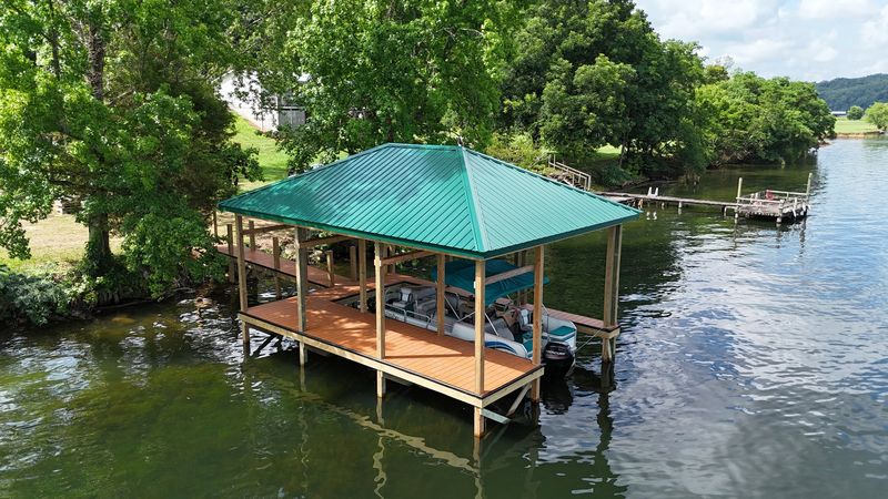 Aerial view of a green metal-roof covered dock with a pontoon in the slip