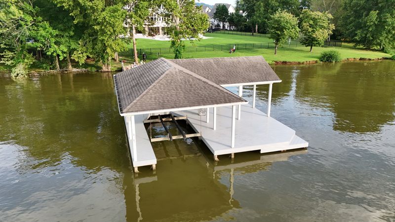 Aerial view of a white-post boathouse with a shingle hip roof and open deck