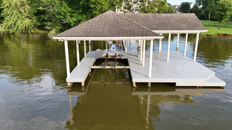 White-post boathouse with a shingle roof, boat lift and wraparound deck