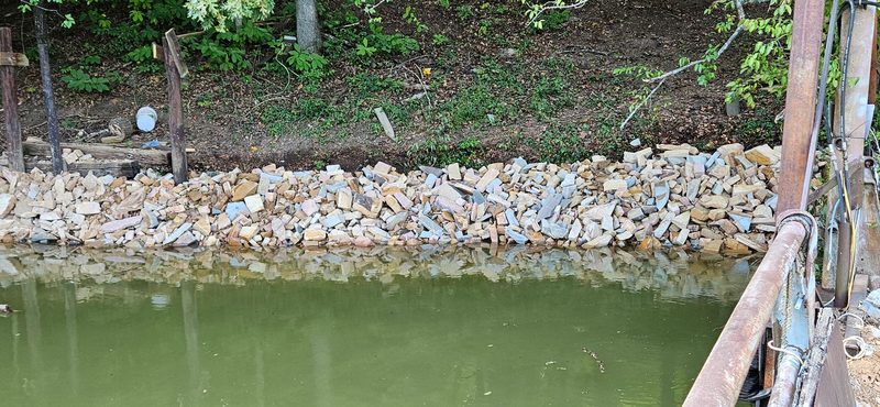 Stacked stone riprap along the water&rsquo;s edge below a wooded lake bank