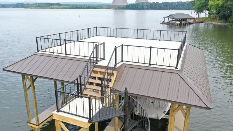 Two-story boathouse with rooftop sundeck and tan metal roof on a Tennessee lake